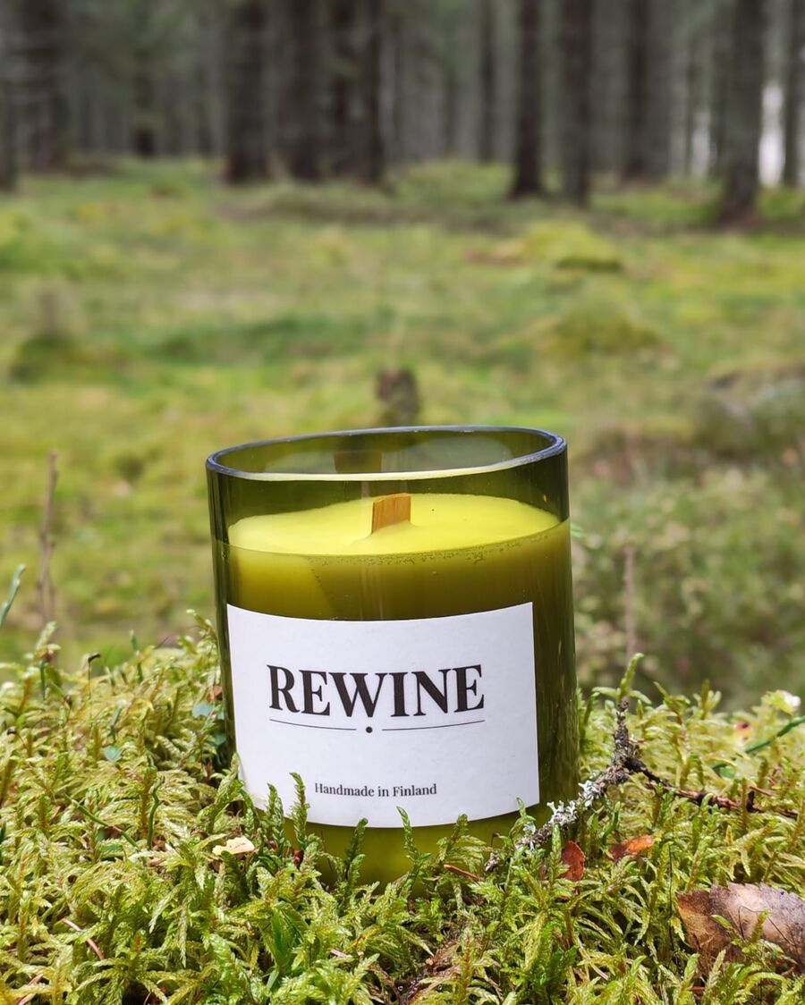 REWINE-kynttilä leikatussa vihreässä viinipullossa sammalmättäällä kuusimetsässä.